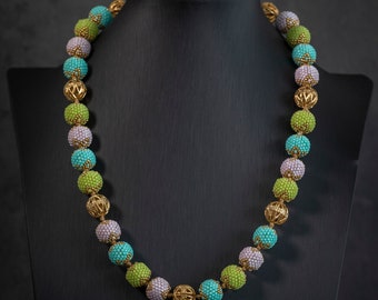 May include: A necklace made of green, blue, and purple beads with gold accents. The beads are round and have a textured surface. The necklace is displayed on a black mannequin.