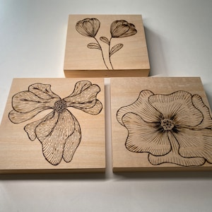 May include: Three wooden wall art pieces with black floral designs. The designs are of different flowers, each with a unique style.