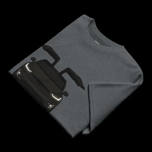 May include: Dark gray t-shirt featuring a black sports car graphic with open doors. The car's headlights are white. The t-shirt is folded, showing the front of the car and part of the shirt's sleeve.