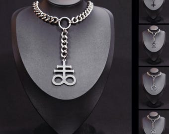 May include: A silver-coloured necklace with a thick chain and a pendant featuring a symbol. The pendant hangs from a smaller chain that connects to a ring. Additional necklaces with different pendants are displayed.