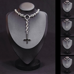 May include: A silver-toned choker necklace with a large inverted cross pendant. The necklace features a chain design with a circular connector and a dangling cross. Additional necklaces with different pendants are displayed on the right.