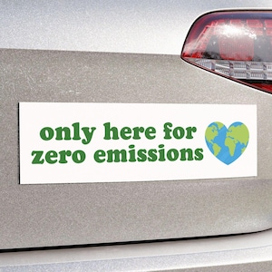 Puede incluir: Una pegatina de parachoques blanca con texto verde que dice "only here for zero emissions" y un corazón azul y verde con un globo terráqueo dentro.