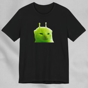 May include: Black t-shirt featuring a green alien cat graphic. The cat has two antennae on its head and is looking directly at the viewer.