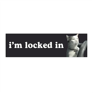 以下が含まれることがあります： 黒い背景に白い文字で「i'm locked in」と書かれた、首輪をした白黒の猫が右を見ている。