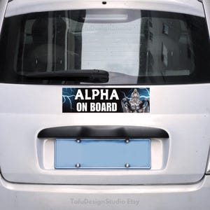 Pu&ograve; includere: Adesivo rettangolare "ALPHA ON BOARD" sul retro di un'auto argentata. Il testo bianco &egrave; accompagnato da un disegno di una creatura muscolosa e fulmini blu.