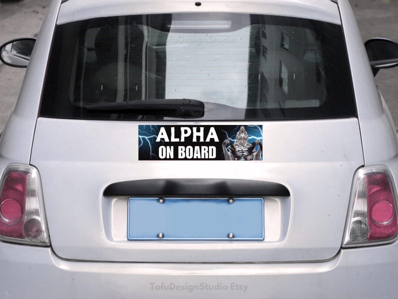 Pu&ograve; includere: Adesivo rettangolare "ALPHA ON BOARD" sul retro di un'auto argentata. Il testo bianco &egrave; accompagnato da un disegno di una creatura muscolosa e fulmini blu.