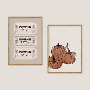 May include: Two framed art prints. One shows three pumpkin patch tickets with the text "PUMPKIN PATCH". The other print displays three brown pumpkins with black outlines on a cream background. Both are in wooden frames.