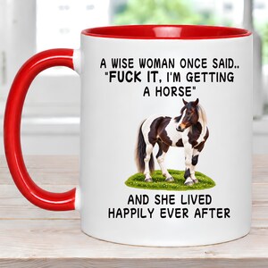 May include: A white ceramic mug with a bright red handle and interior rim. The front features a black printed quote: A WISE WOMAN ONCE SAID.. "FUCK IT, I'M GETTING A HORSE" AND SHE LIVED HAPPILY EVER AFTER, centered above and below a brown and white horse.