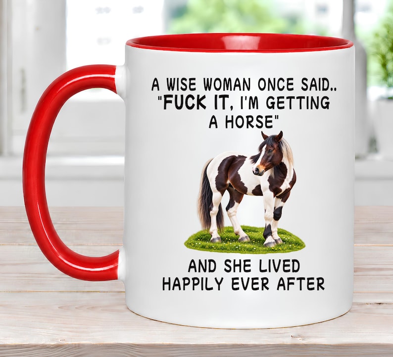 May include: A white ceramic mug with a bright red handle and interior rim. The front features a black printed quote: A WISE WOMAN ONCE SAID.. "FUCK IT, I'M GETTING A HORSE" AND SHE LIVED HAPPILY EVER AFTER, centered above and below a brown and white horse.