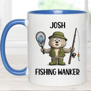 May include: White ceramic mug with a blue handle and rim, featuring a cartoon bear dressed as a fisherman. The bear holds a fishing net with a fish and a fishing rod. Text on the mug reads "JOSH FISHING WANKER."