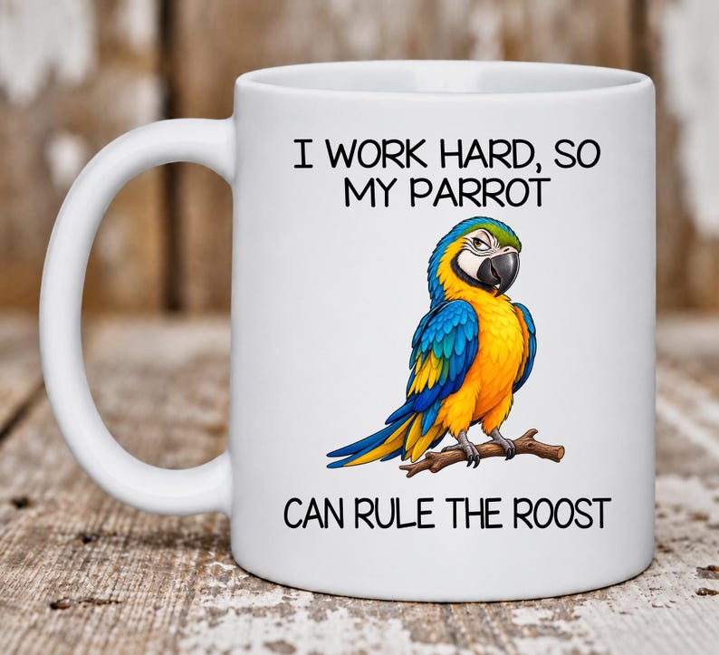 May include: A white ceramic mug featuring a colorful illustration of a blue and yellow macaw parrot perched on a brown branch. The text printed on the mug reads: I WORK HARD, SO MY PARROT CAN RULE THE ROOST. The mug has a curved handle on the left side.