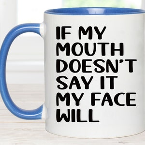 May include: White ceramic coffee mug with a blue rim and handle. The mug has black text that reads "If my mouth doesn't say it my face will."