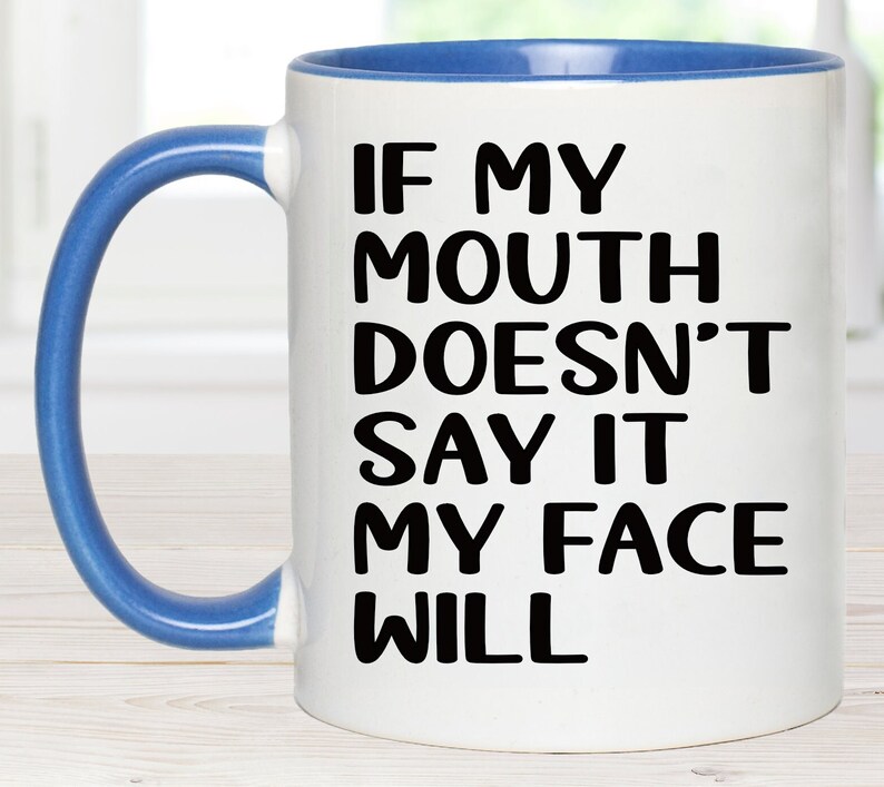 May include: White ceramic coffee mug with a blue rim and handle. The mug has black text that reads "If my mouth doesn't say it my face will."
