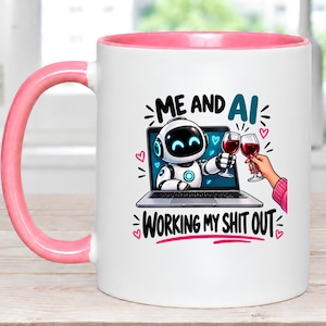 May include: A white ceramic mug with a pink handle and interior rim. The front features a graphic of a robot on a laptop screen clinking a wine glass with a hand. The text reads ME AND AI WORKING MY SHIT OUT, surrounded by small pink hearts.