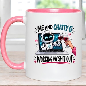 May include: A white ceramic mug with a pink handle and interior rim. The graphic features a white robot on a laptop screen clinking a wine glass with a person. The text reads ME AND CHATTY G WORKING MY SHIT OUT, surrounded by small pink hearts.