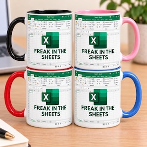 May include: Four ceramic mugs featuring a white background with a printed Microsoft Excel spreadsheet interface and the green Excel logo. The text "FREAK IN THE SHEETS" is printed in dark green. Each mug has a different coloured handle: black, pink, red, and blue.