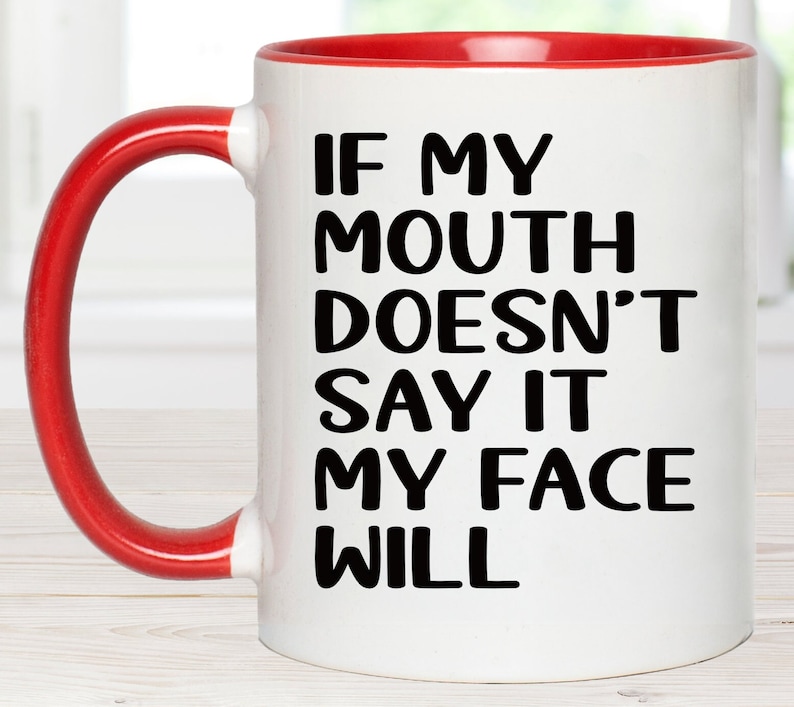May include: White ceramic coffee mug with a red rim and handle. The mug has black text that reads "If my mouth doesn't say it my face will."