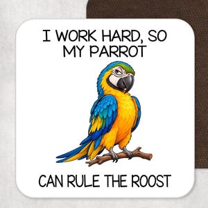 May include: A square white coaster featuring a colorful blue and yellow macaw parrot perched on a brown branch. The text above the bird reads I WORK HARD, SO MY PARROT and the text below the bird reads CAN RULE THE ROOST in black font.