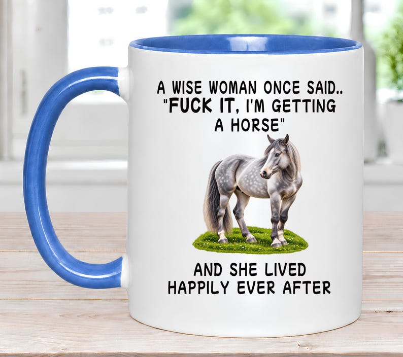 May include: A white ceramic mug with a blue interior and handle. The front features a dapple gray horse standing on green grass, with the black text: A WISE WOMAN ONCE SAID.. "FUCK IT, I'M GETTING A HORSE" AND SHE LIVED HAPPILY EVER AFTER.