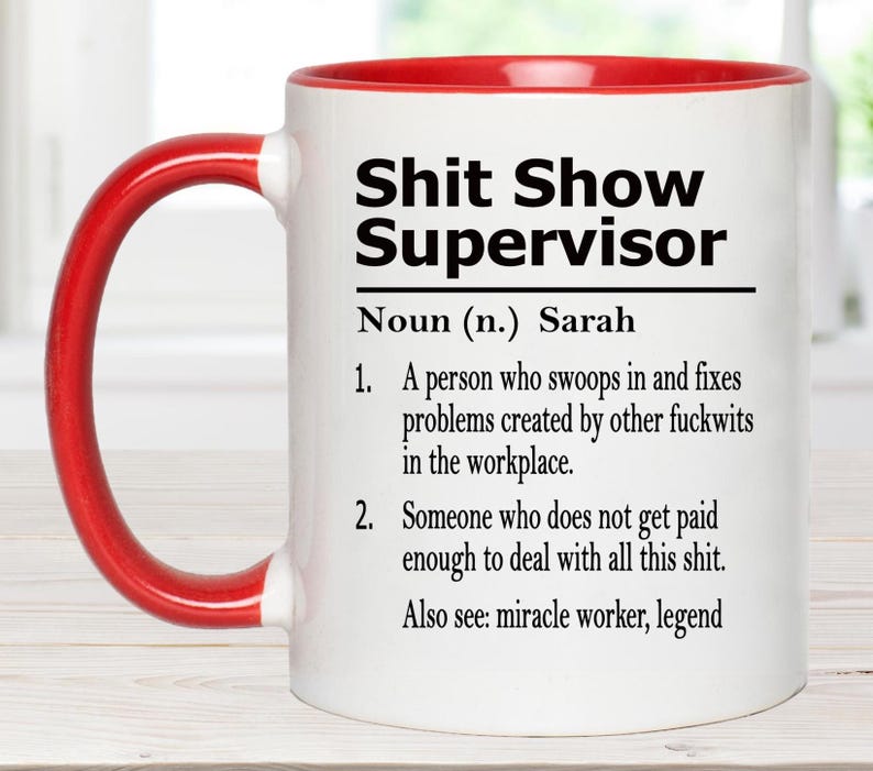 May include: A white ceramic mug with a red handle and interior rim. The front features black text reading: Shit Show Supervisor, Noun (n.) Sarah, 1. A person who swoops in and fixes problems created by other fuckwits in the workplace. 2. Someone who does not get paid enough to deal with all this shit. Also see: miracle worker, legend.