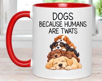 May include: A white ceramic mug with a bright red handle and interior rim. The front features black text that reads DOGS BECAUSE HUMANS ARE TWATS above a stacked illustration of four sleeping puppies in shades of brown, black, and tan.