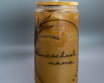 May include: A glass tumbler with a bamboo lid and a clear glass straw. The tumbler is filled with iced coffee and has a black and white design that says "Homeschool mama".