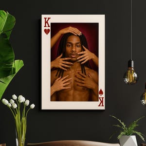 Puede incluir: Una impresión artística enmarcada que presenta un retrato de una persona con rastas, con manos tocando su rostro y pecho. La obra de arte está enmarcada con un diseño de carta de juego, con el símbolo del Rey de Corazones en la parte superior e inferior. El fondo es rojo oscuro.