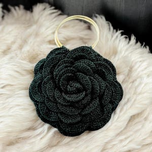 May include: A dark green, crocheted rose-shaped handbag with a gold ring handle.