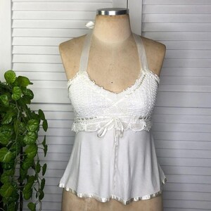 May include: White halter top with a textured bodice and a flowing bottom. The top features a delicate lace trim and a ribbon tie at the waist. The halter straps are made of a sheer material. The bottom hem is trimmed with a satin ribbon.