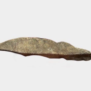 May include: A long, thin, gray-brown stone with a smooth, slightly curved surface. The stone has a natural, rough texture.