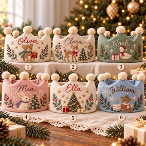 May include: Six fabric crowns with pom-pom trim, each featuring embroidered names and holiday motifs including bears, deer, ducks, rabbits, and Christmas trees. The crowns are numbered one through six and display the names Oliver, Clara, Noah, Mia, Ella, and William.