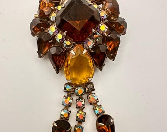 May include: A large, vintage brooch with a cluster of amber and iridescent rhinestones. The brooch has a dangling tassel of smaller rhinestones.
