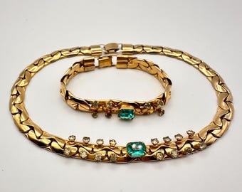 May include: A gold chain necklace and bracelet set with green and clear rhinestones. The necklace and bracelet have a braided chain design.