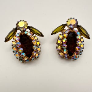 Puede incluir: Un par de pendientes vintage con una piedra ovalada marrón rodeada de piedras de cristal iridiscentes y tres piedras verdes en cada pendiente.