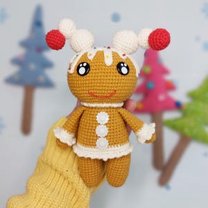 Puede incluir: Un juguete de jengibre de crochet con glaseado blanco, decoraciones de caramelo rojo y blanco y ojos negros. El juguete lleva una falda de crochet blanca y tiene un cuerpo de crochet marrón.