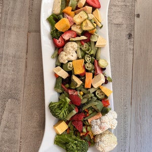 May include: A white platter filled with a variety of dried fruits and vegetables, including strawberries, broccoli, cauliflower, and green beans.

“Premium freeze-dried bird food by Runzas made with real fruits and vegetables for parrots”