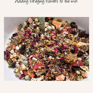 May include: A close-up of a bowl filled with a colorful mix of dried fruits, vegetables, and flowers. The mix includes dried orange slices, dried apple pieces, dried cranberries, dried rose petals, and other dried flowers.