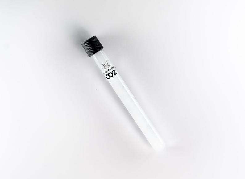 Puede incluir: Un tubo de ensayo transparente con una tapa negra. El tubo tiene una etiqueta blanca con el texto "LASMAGEN CO2" impreso en negro. El tubo est&aacute; inclinado sobre un fondo blanco.