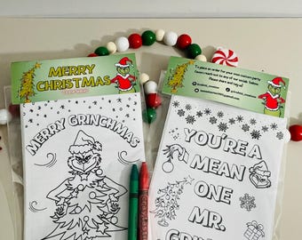 Puede incluir: Dos bolsas de plástico transparente con páginas para colorear con temática navideña y crayones. Una bolsa dice "Merry Grinchmas" y la otra "You're a Mean One Mr. Grinch!". Se incluyen crayones rojos y verdes.