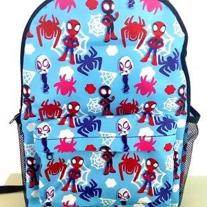 May include: A light blue backpack featuring a repeating pattern of Spider-Man characters, spiders, and spiderwebs. The backpack has a front pocket, black mesh side pockets, and black trim. The design includes red, white, and black elements.