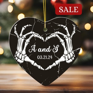 May include: Black heart-shaped ceramic ornament with white skeletal hands forming a heart shape. The ornament has the text "A and S" and the date "03.21.24" in white.