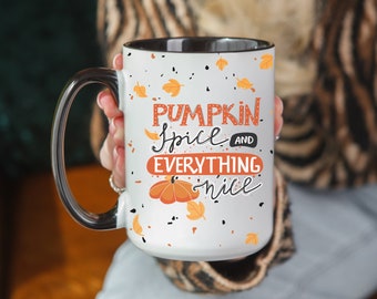May include: White ceramic mug with a black rim and handle. The mug has a black and white speckled background with a pumpkin spice and everything nice design in orange, black, and white.