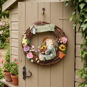 May include: A circular grapevine wreath featuring a green sign that reads "WELCOME TO MY GARDEN" with a small birdhouse attached. A fabric doll wearing a patterned outfit sits in the center, surrounded by artificial pink, yellow, and purple flowers.
