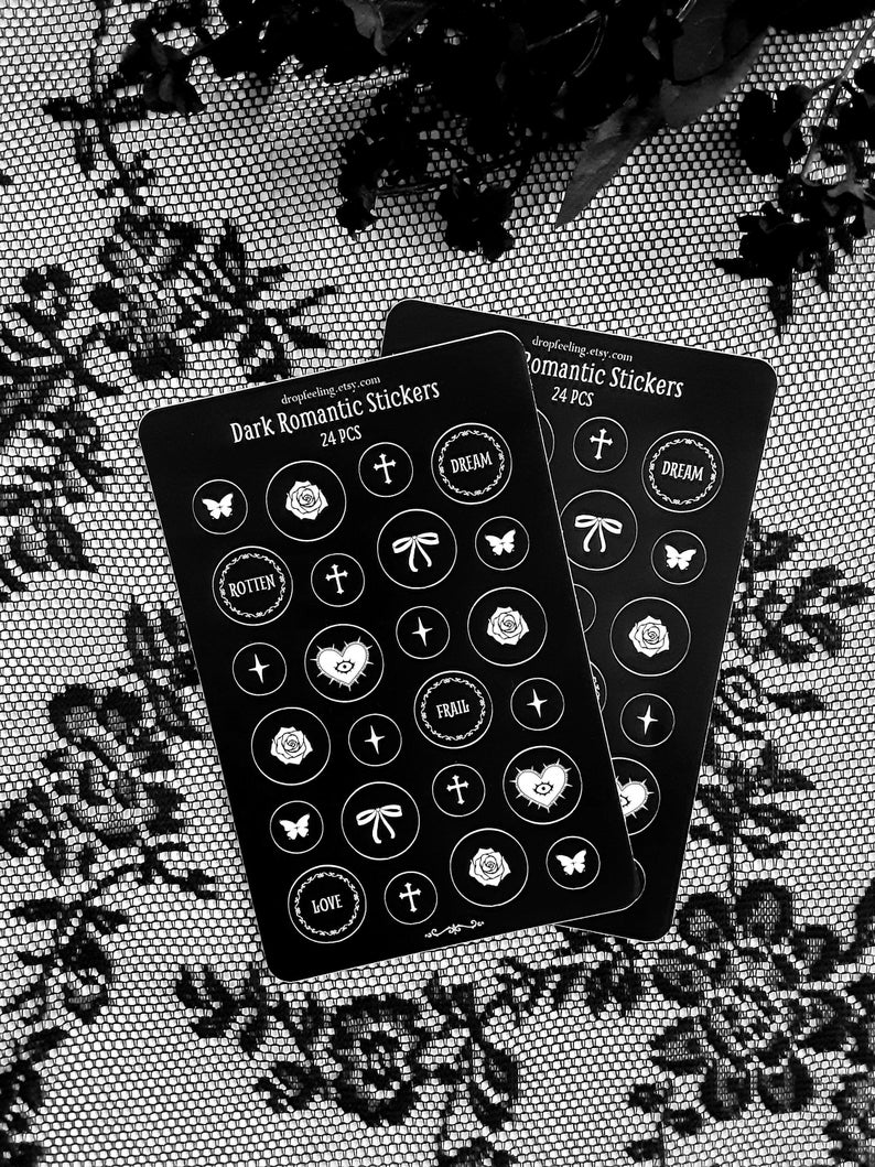 May include: Two sheets of black sticker paper with white designs. The stickers feature various dark romantic themes, including roses, butterflies, hearts, crosses, and text like "Dream", "Rotten", "Frail", and "Love".