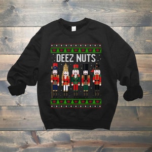 May include: Black Christmas sweater with a festive design featuring a row of nutcracker figurines and the text "DEEZ NUTS".