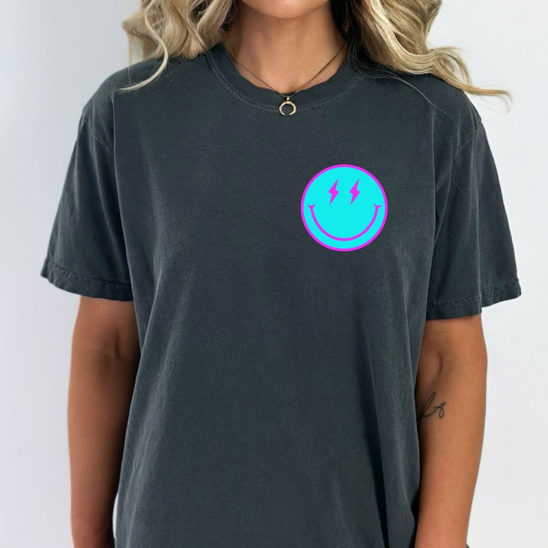 May include: A black t-shirt with a turquoise blue smiley face graphic with pink lightning bolts.