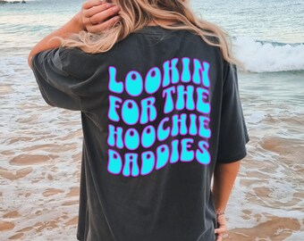 Puede incluir: Una camiseta negra con un gráfico azul y morado que dice "Lookin for the Hoochie Daddies".
