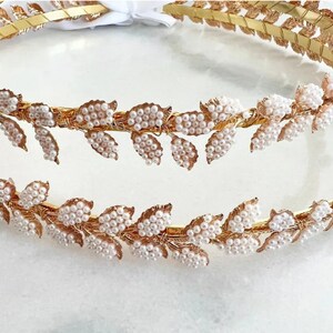 May include: Two gold leaf headbands with pearl accents. The headbands are layered on top of each other.
