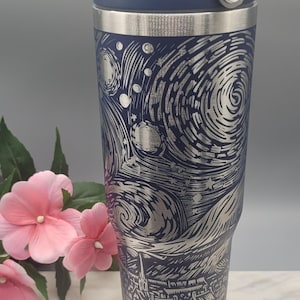 May include: A navy blue stainless steel travel mug with a silver, etched design inspired by Van Gogh's "Starry Night." The mug has a dark blue lid and a silver rim. The design features swirling stars, a village, and a crescent moon.