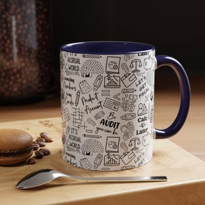 May include: A white ceramic coffee mug with a blue rim and handle. The mug features a black and white design of accounting-related doodles and text, including "Make it Account", "Be Audit you can be", and "Let's Get Fiscal".